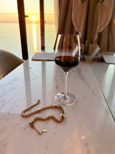 Zlatý náhrdelník zobrazen při západu slunce se sklenkou červeného vína