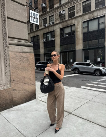 Stylová žena stojící na newyorské ulici v minimalistickém outfitu – černý top s tenkými ramínky, béžové volné kalhoty, černá pletená kabelka z veganské kůže a špičaté podpatky. Nadčasový chic streetstyle look s nádechem luxusu. kabelka inspirovana bottega veneta