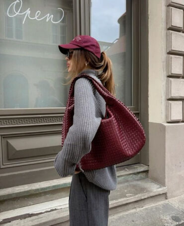 Stylová bordó pletená shopper kabelka z veganské kůže, nošená přes rameno v podzimním street style outfitu s šedým svetrem