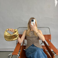 blonde woman holding a gold woven knot clutch bag made from vegan leather inspired by designer bottega veneta