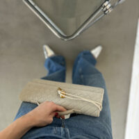 Luxusní minimalistické psaníčko z vegan kůže v taupe odstínu, nošené jako crossbody kabelka nebo elegantní clutch.